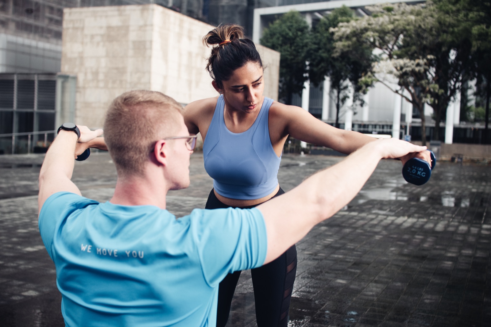 A FitBeat coach guiding a client through a dumbbell raise outdoors in Singapore
