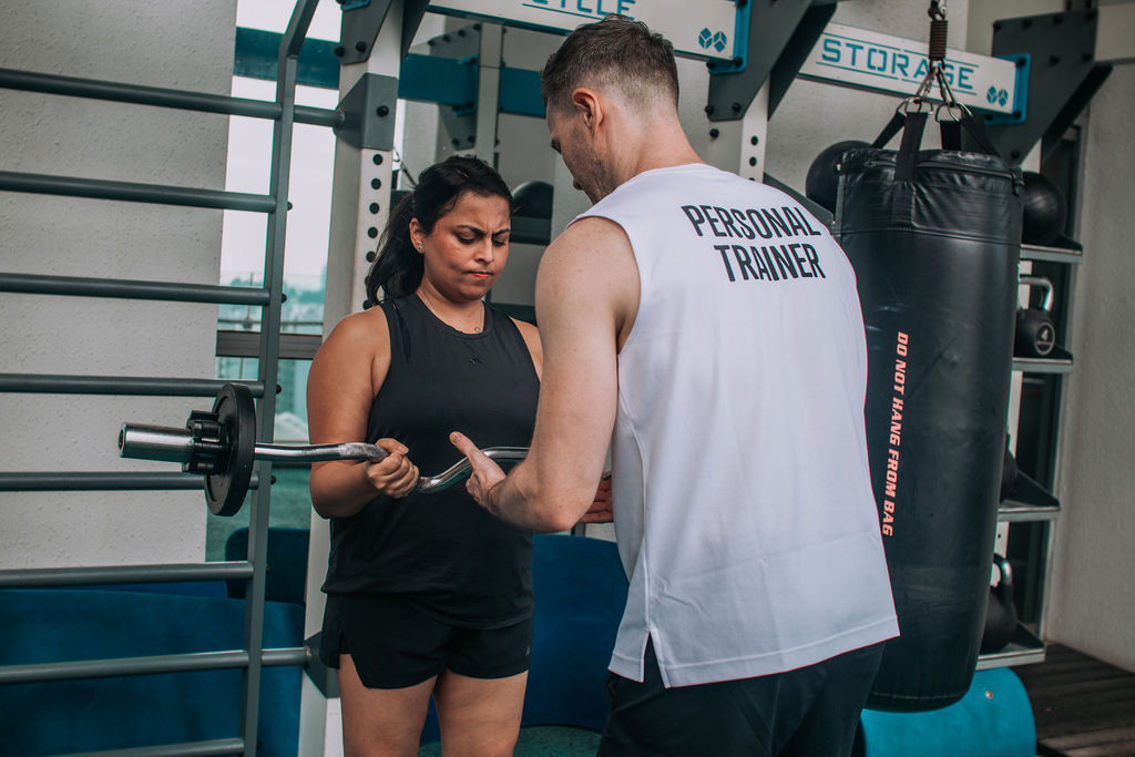 A FitBeat coach checking a client’s grip and set-up on a barbell in a condo gym