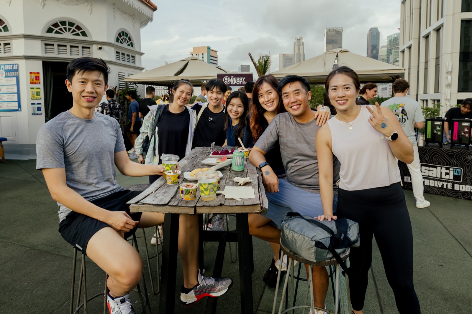 Seven people around a high wooden table with açaí cups and cans, the rooftop turret and the skyline behind them